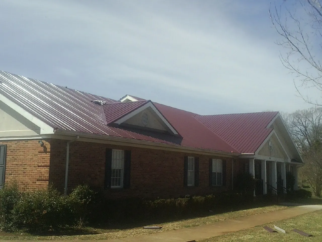 Red metal roof with gabled entries on a long brick building, from a Hail Damage Roof Repair job in Kanarraville