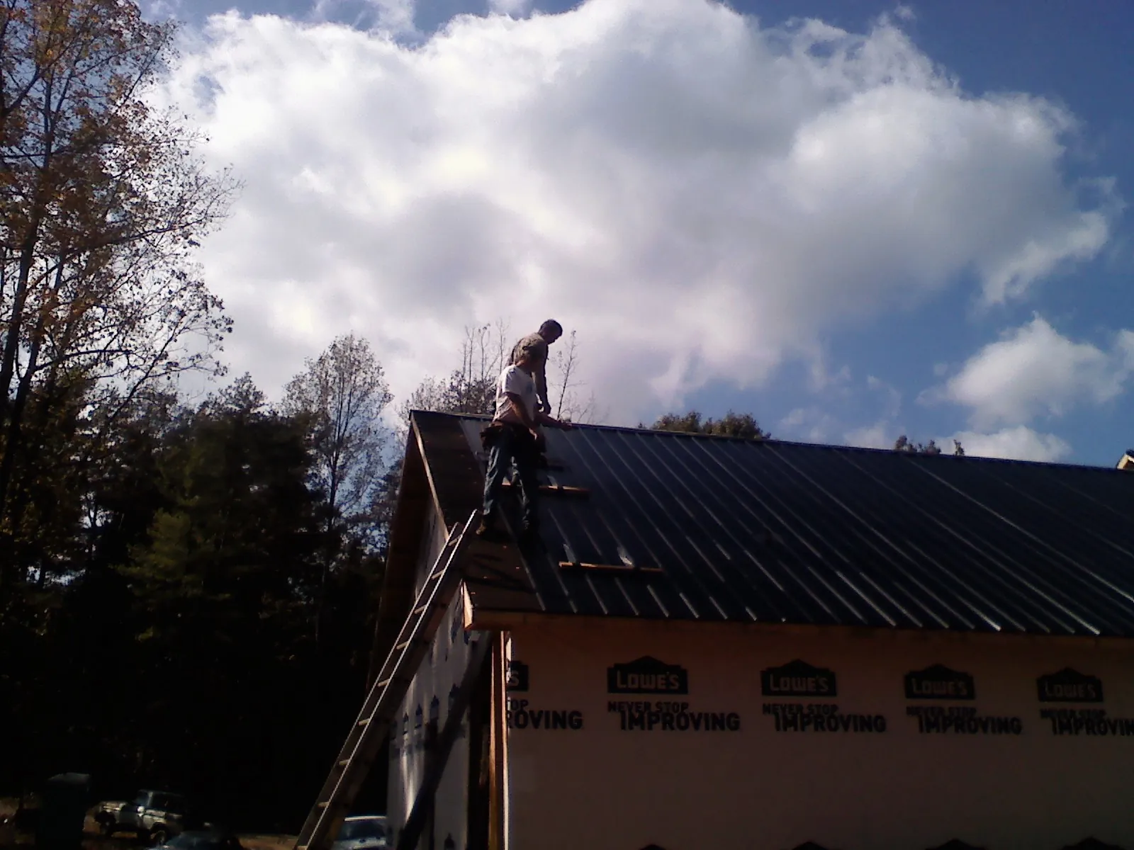 Roofer fastening dark metal panels high against a cloudy sky, from a Roof Inspection job in Kanarraville