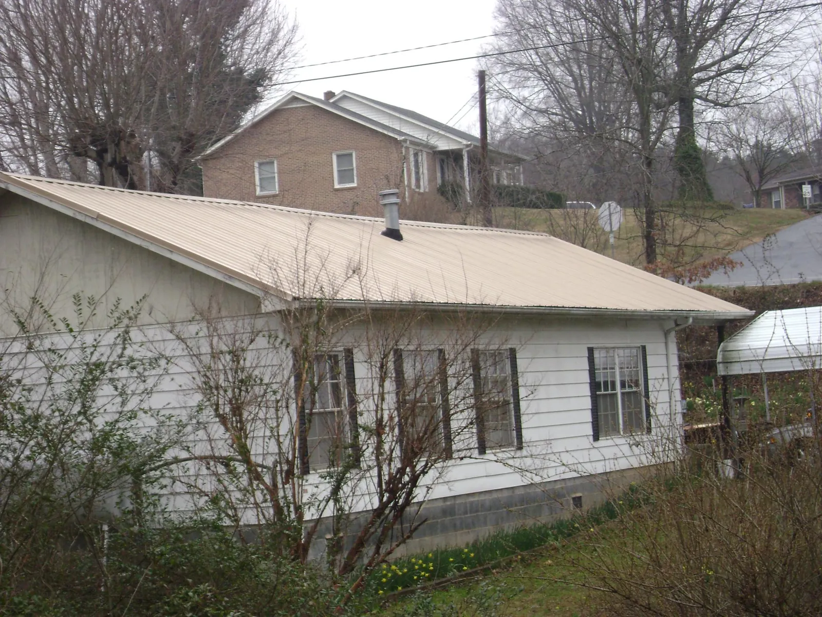 Tan metal roof on a white sided house set into a hillside — Commercial Roofing by Roofing Brothers in Kanarraville